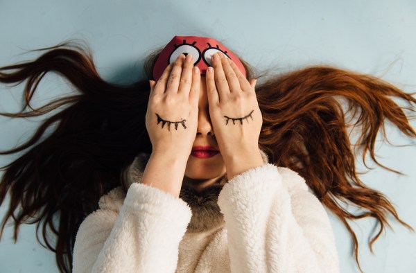 Young beautiful girl in a sweater with a deer and a sleep mask lying down on white background.