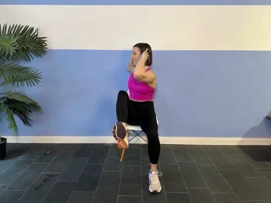 Personal trainer demonstrating alternating elbow to knee rotations on a chair