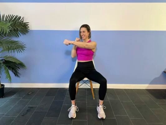 Personal trainer demonstrating cross body punch while sitting on chair