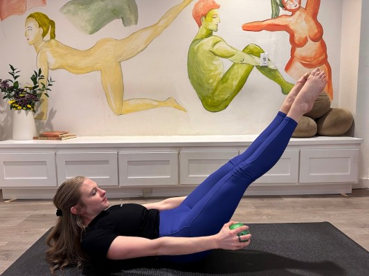 Pilates instructor demonstrating Pilates hundred with a prop