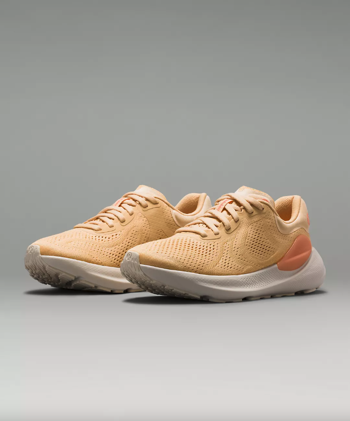 A pair of orange sherbet colored running shoes against a light gray background.