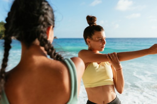 Two female friends warming up before a quick beach workout