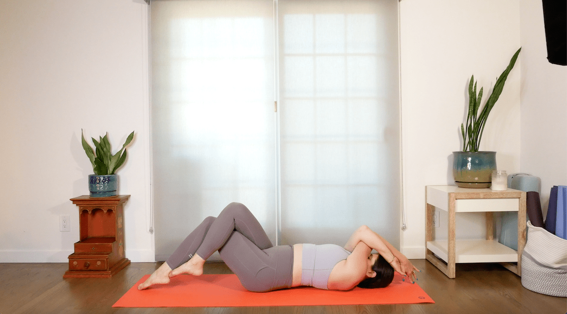 yoga teacher demonstrates how to perform the spine eagle pose in yoga, with her back on a mat
