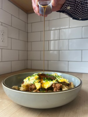 Close up image of bowl of scrambled pancakes with chorizo, eggs, and cheese with maple syrup being poured on top