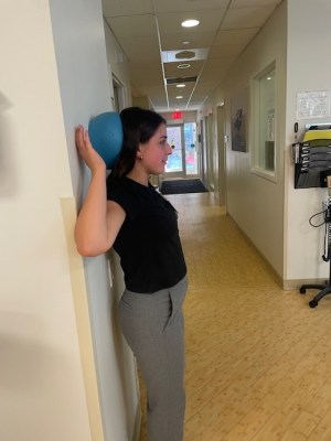 Physical therapist demonstrating wall angel with soft object behind neck