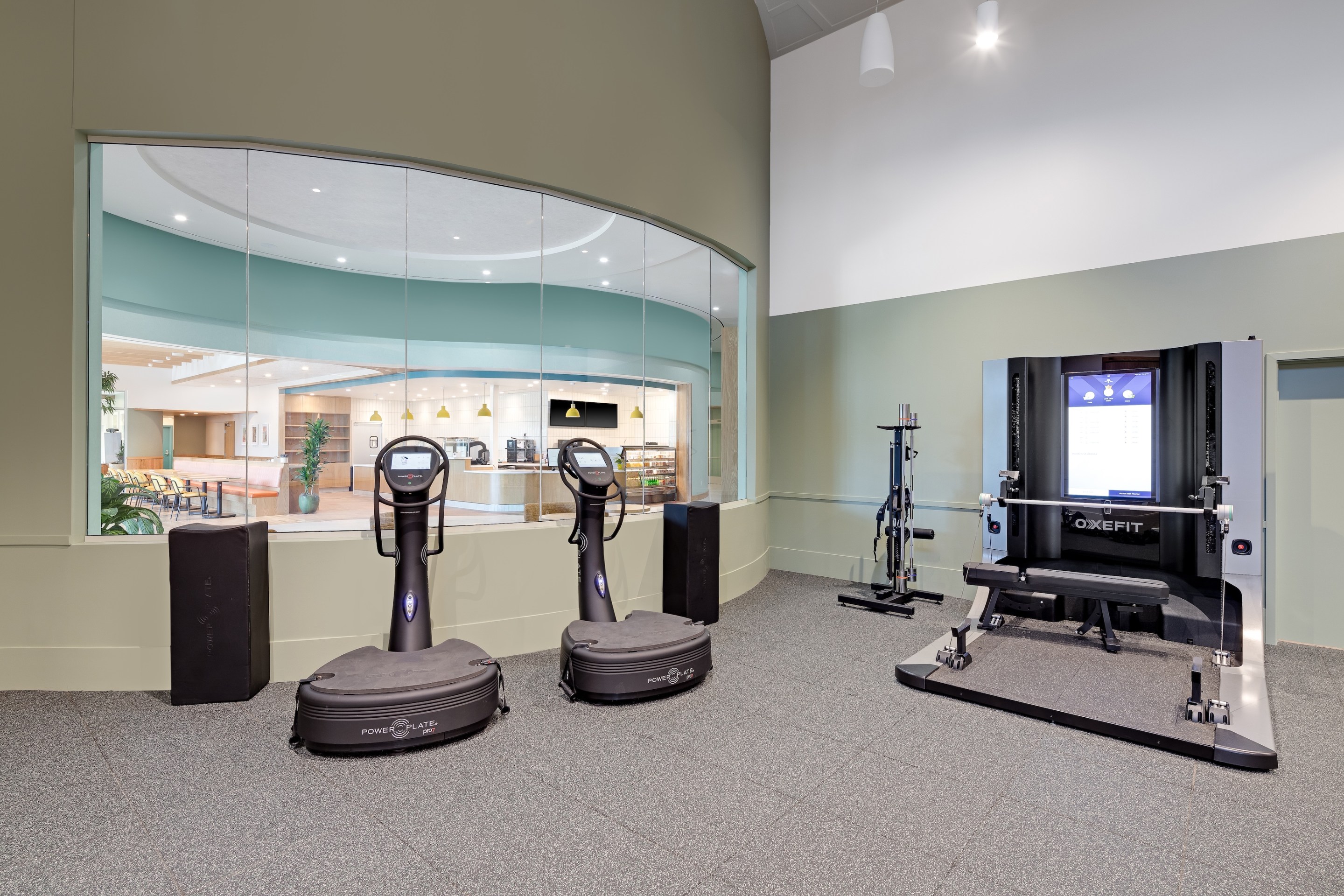 A gym with high tech fitness machines with a window to a cafe.