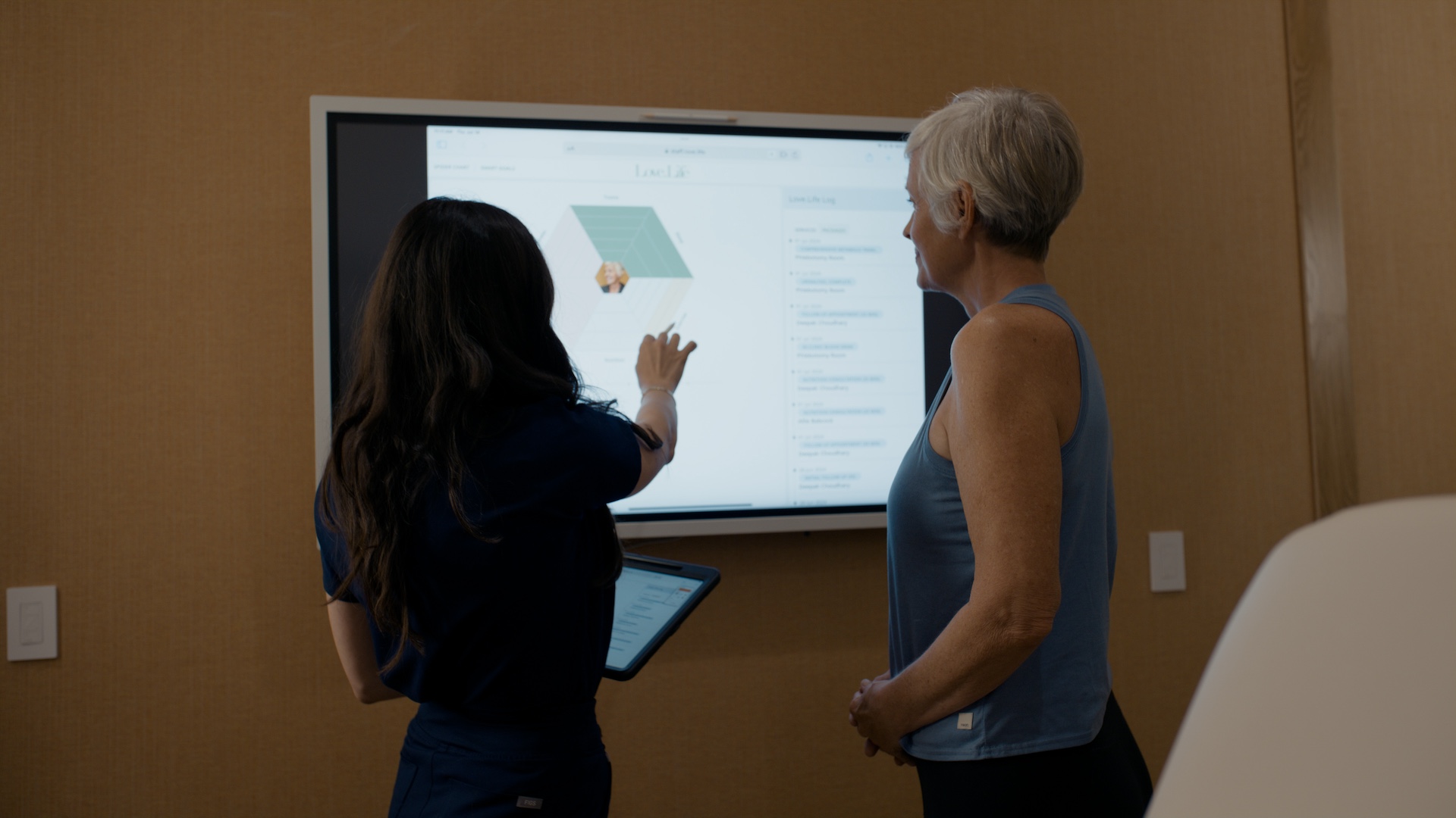 A doctor showing a woman a graph with her healthcare information on a large television screen.