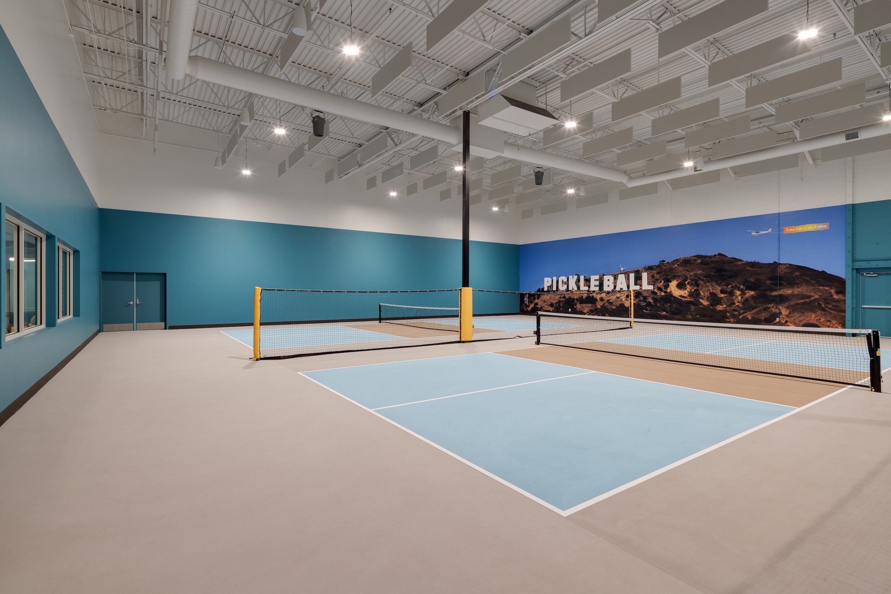 Two light blue pickleball courts with a mural of the Hollywood sign, that instead says "Pickleball," in the background.