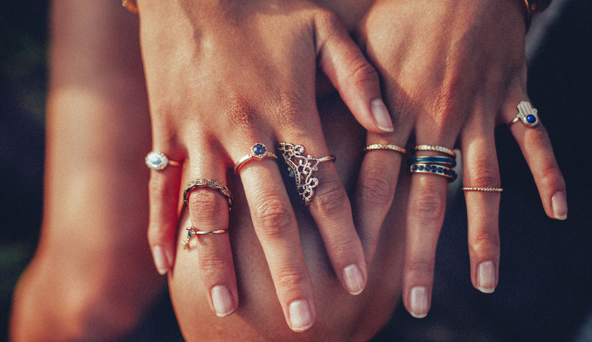 Cropped closeup of a boho girl's hands with many rings on her fingers, in gold and silver with dark blue stones. This photo is being used in an article about gold-filled vs. gold-plated jewelry.