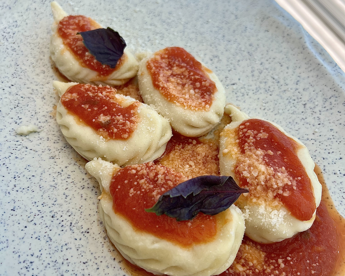 Five Culurgiones, a local Sardinian dish of stuffed pasta, topped with red sauce on a plate.