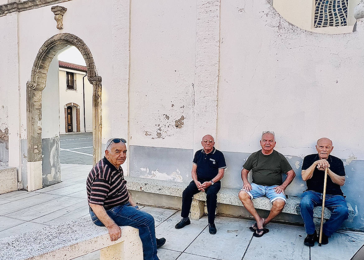 four older gentlemen socialize together outdoors in Sardinia