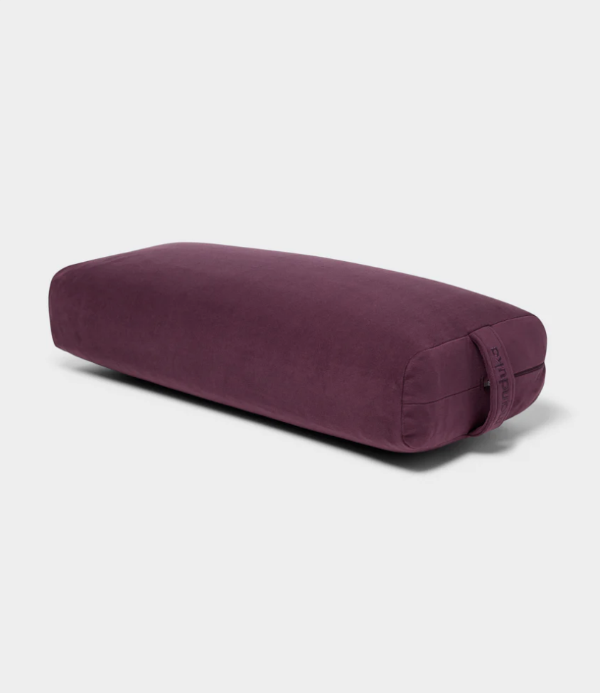 Photo of purple Manduka brand yoga bolster on gray background