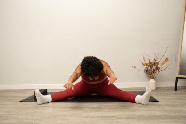 Pilates instructor demonstrating seated spine stretch with elevated hips