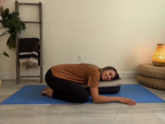 Yoga teacher demonstrating supported child's pose with yoga bolster