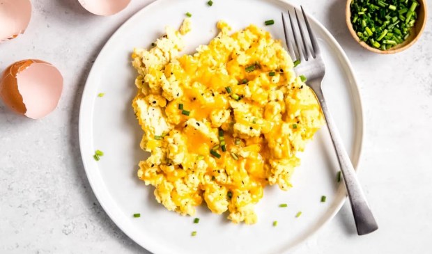 a close-up shot of a plate of cottage cheese scrambled eggs and a small side of chopped chives