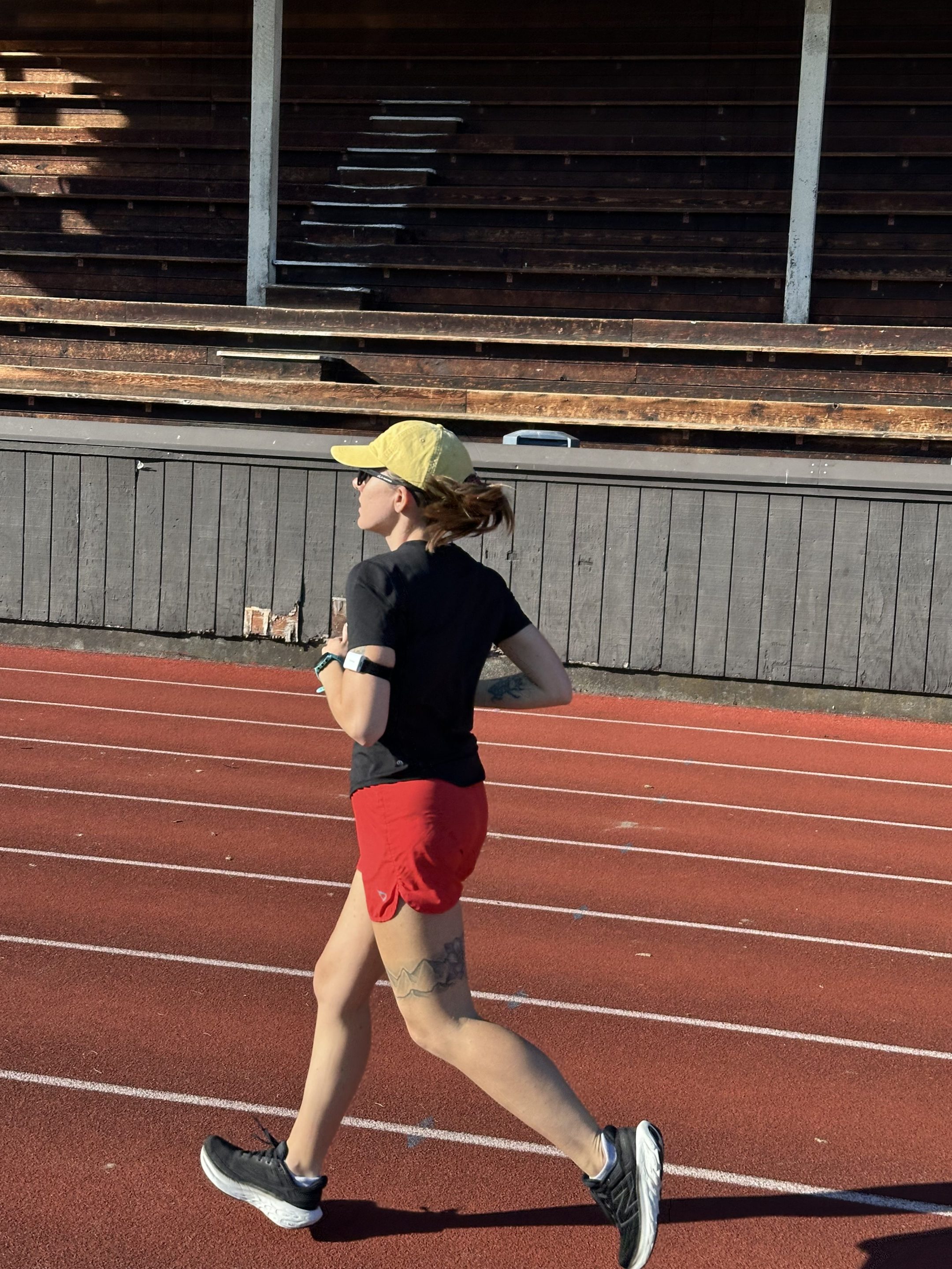 woman wearing a hat running on a track wearing the hDrop hydration wearable