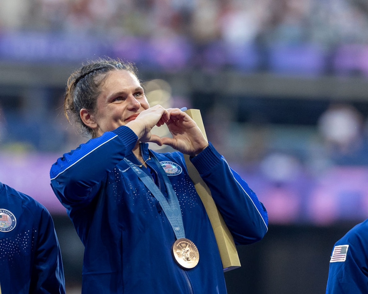 Rugby player Ilona Maher making a heart with her hands wearing an Olympic bronze medal around her neck