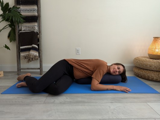 Yoga teacher demonstrating restorative twist with yoga bolster