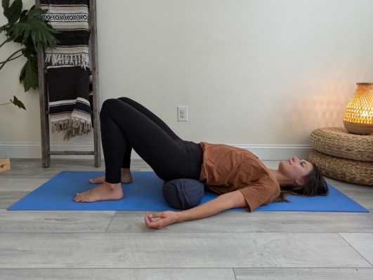 Yoga teacher demonstrating supported bridge pose with yoga bolster 