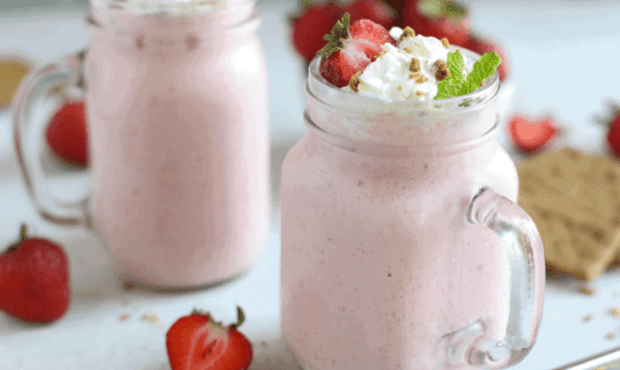 strawberry cheesecake smoothies in see-through glass mugs with whipped cream and sliced strawberries on top