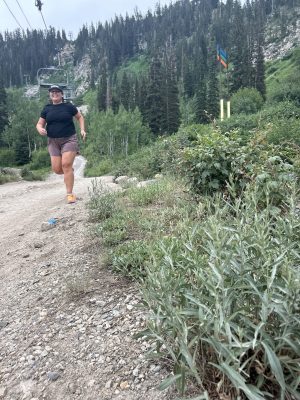 A woman running on a trail in front of a ski lift.