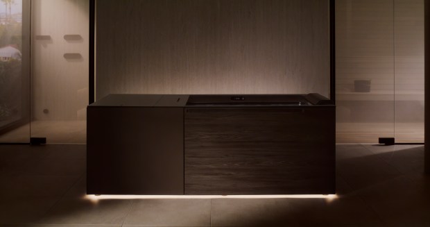 A dark wood tub with an underlit bottom, the Kohler x Remedy Place Ice Bath, seen in a spa-like bathroom.