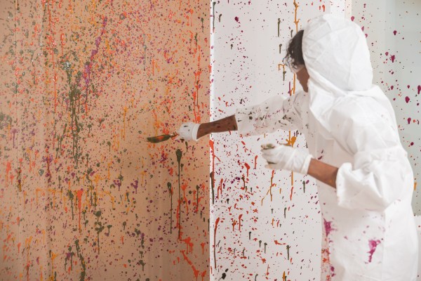 close up of a person wearing a white protective suit while throwing paint with a paintbrush at Therapaint studios in Nashville, Tennessee