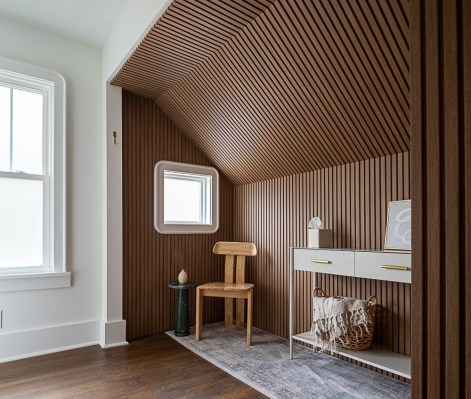 a well-lit room with wood paneling on the walls to the right and a white wall with a window to the left. A chair, rug, and white sleek side table decorate the paint throwing room at Therapaint.