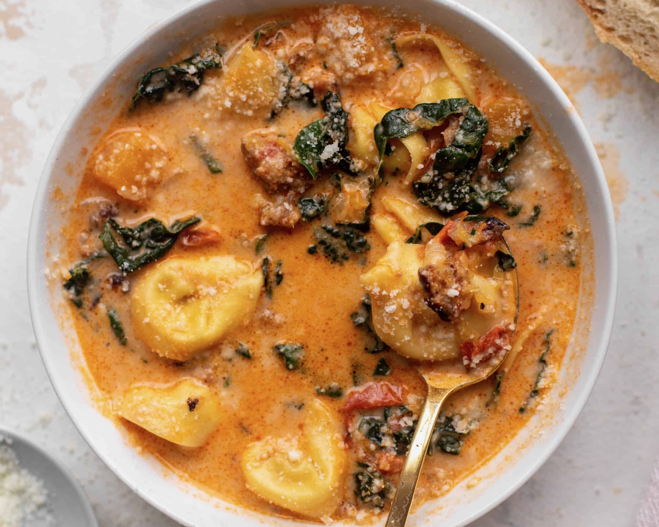 In a white bowl, orange colored soup with green and tortellini