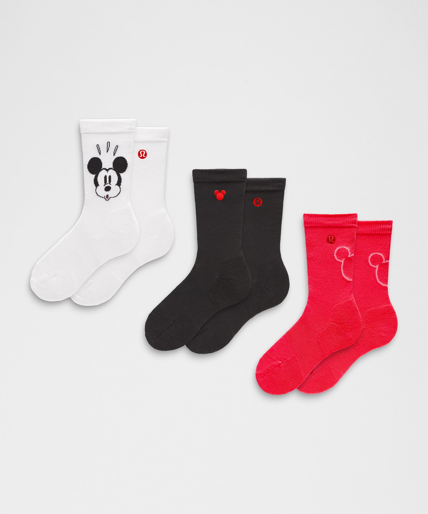 Three pairs of socks, one in white with a Mickey Mouse face on it, one in black, and one in hot pink.