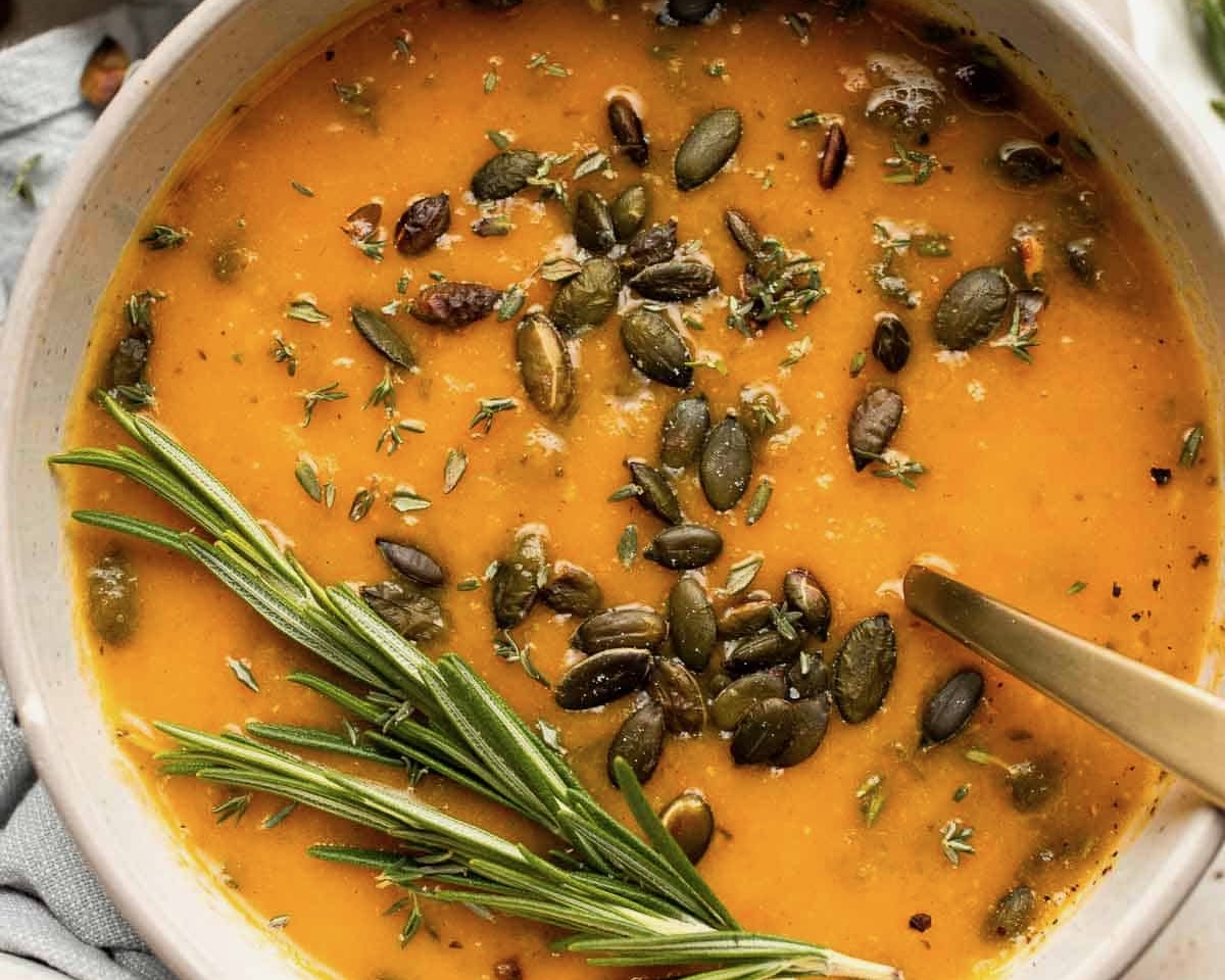 orange soup with a prig of thyme, spices, and pumpkin seeds on top