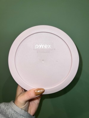 a pink silicone covered circular storage container is held up against a green background